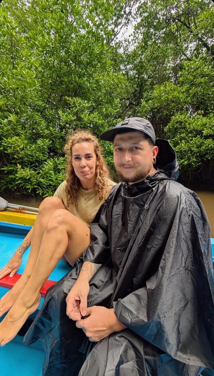 Two guests in a blue safari boat, one wrapped in a rain poncho during a passing shower